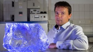 Glaschemiker Prof. Dr. Lothar Wondraczek neben einem Glasblock bestehend aus hochreinem Borosilikatglas im Labor.